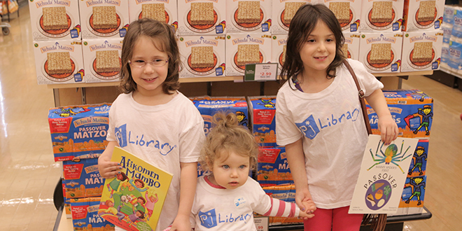 Sisters Dalia Left and Lila Sukert hold on to Aviva Konstantinosvky boosting the PJ library program in front of Yehuda Matzos display